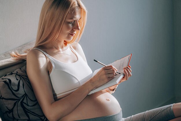 Mulher grávida sentada no sofá e fazendo uma lista de compras para seu bebê