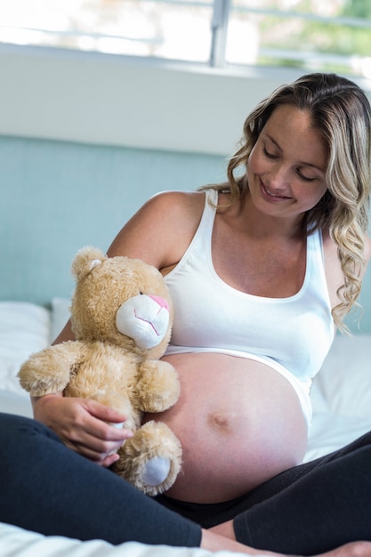 Foto mulher grávida, sentando, com, um, urso teddy, ligado, dela, cama