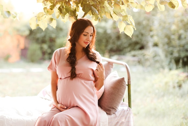 Mulher grávida sorridente com um elegante vestido rosa segurando a barriga