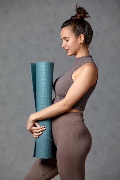 Mulher grávida sorridente em roupas esportivas prontas para ginástica matinal ou exercício Fêmea jovem feliz segue um estilo de vida saudável durante a gravidez segura tapete de ioga para Pilates ou alongamento