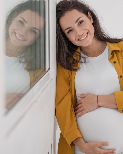 Mulher grávida sorridente olhando posando ao lado da janela