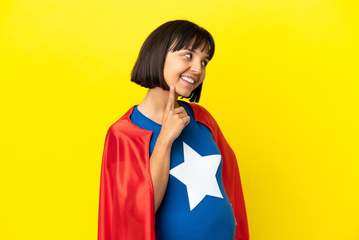 Foto mulher grávida super-heroína isolada em um fundo amarelo pensando uma ideia enquanto olha para cima