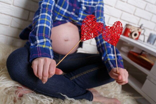 Mulher grávida tem dois corações de brinquedo nas mãos