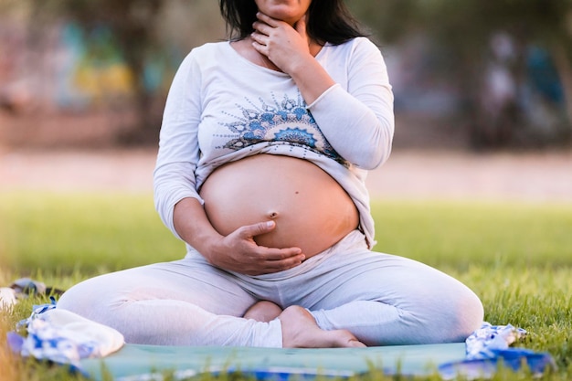 Mulher grávida toca sua barriga sentada em pose de ioga