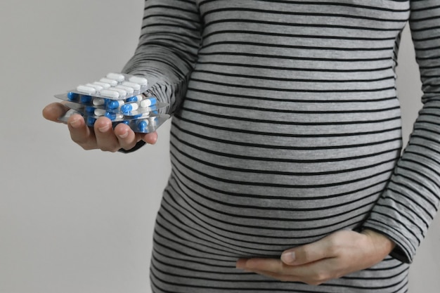 Mulher grávida tocando sua barriga e segurando os comprimidos em um espaço de cópia de plano de fundo cinza