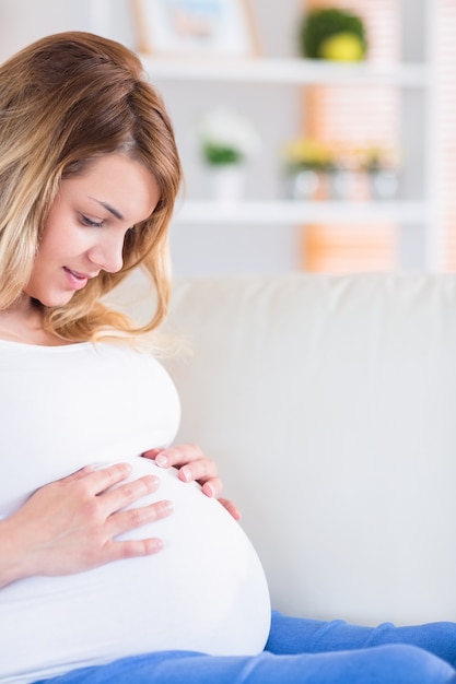 Mulher gravida tocando sua barriga no sofá