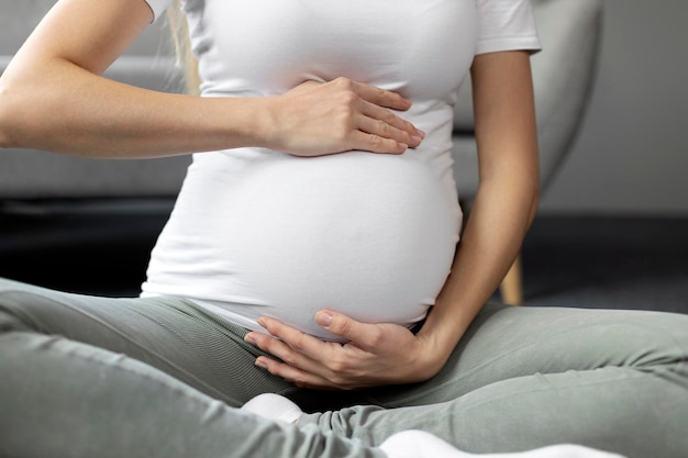 Mulher grávida tocando sua barriga sentada em pose de lótus em casa. Gravidez, maternidade, vida nova