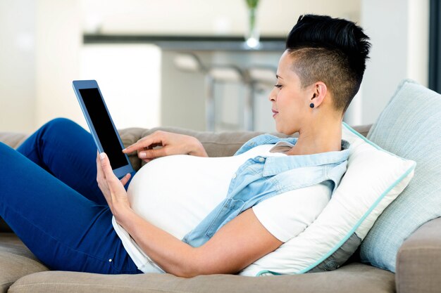 Mulher grávida usando tablet digital enquanto relaxa no sofá na sala de estar