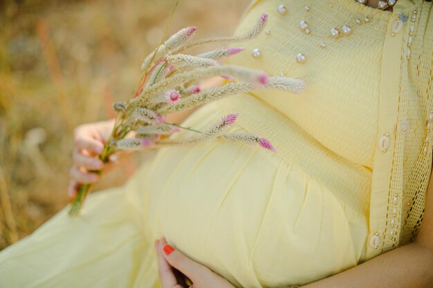 Mulher grávida, usando vestido amarelo claro, segurando nas mãos o buquê de flores da margarida.