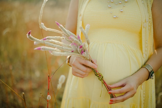 Mulher grávida, usando vestido amarelo claro, segurando nas mãos o buquê de flores da margarida.