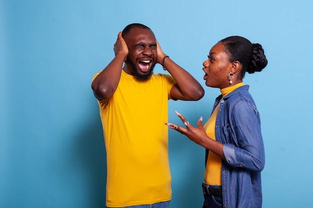 Mulher gritando com homem cobrindo os ouvidos para parar a discussão, expressando frustração. casal infeliz brigando e gritando no estúdio, tendo problemas de relacionamento. pessoas chateadas em conflito.