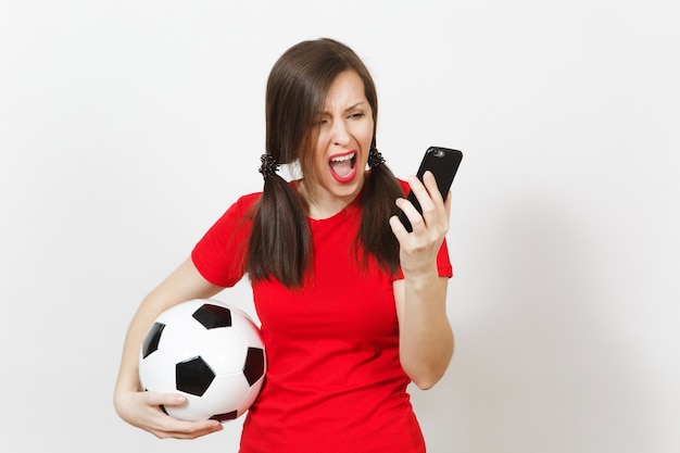 Mulher gritando com raiva jovem europeu, fã de futebol ou jogador de uniforme amarelo falar no celular, segurar uma bola de futebol isolada no fundo branco. Esporte, jogue futebol, conceito de estilo de vida saudável.