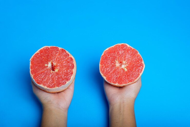 Foto mulher han segurando uma toranja rosa cortada isolada em fundo azul citrus isolado