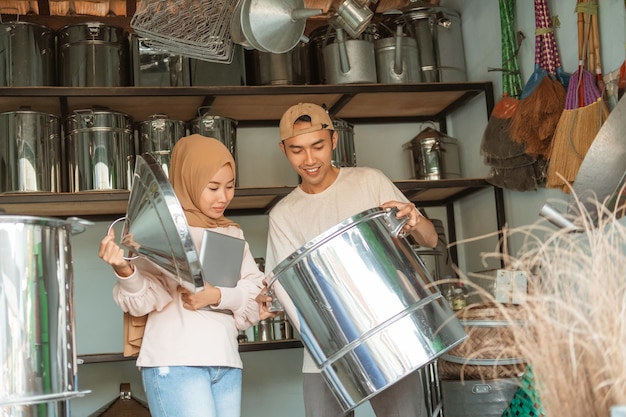 Mulher hijab em pé usando um tablet quando abre uma panela grande com tampa e um vendedor segurando uma panela grande na loja de eletrodomésticos