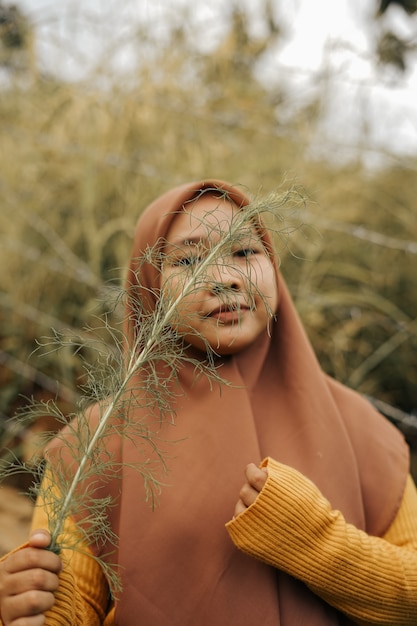 Foto mulher hijab segurando planta em área de jardim