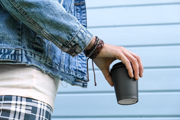 Mulher hippie usando pulseiras de couro boho no pulso e jaqueta jeans, segurando um copo de papel para viagem com café, vício em cafeína, horário de verão.