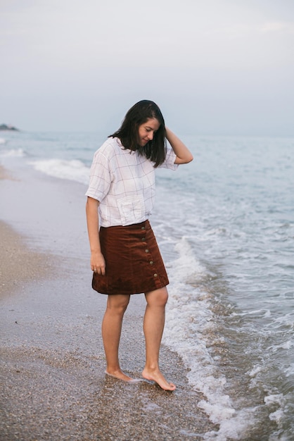 Mulher hipster despreocupada andando descalça na praia com ondas do mar desfrutando de uma noite tranquila