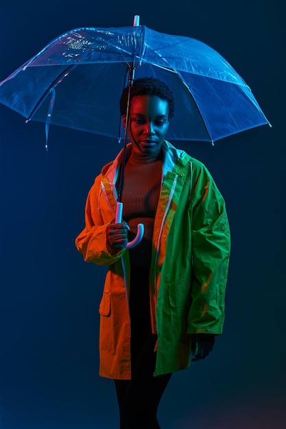 Mulher hipster em capa de chuva com guarda-chuva em luz neon