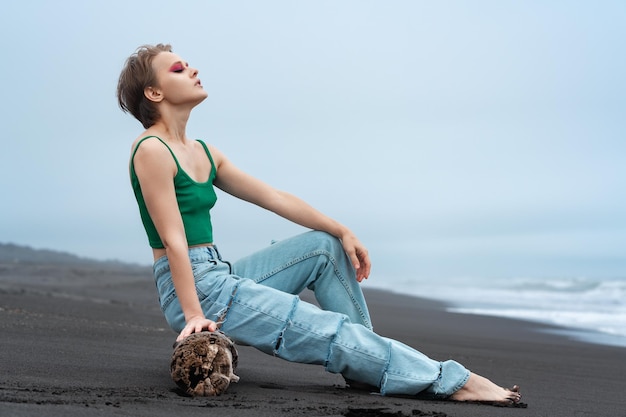 Mulher hipster incrível com os olhos fechados, recostando-se no tronco na praia de areia preta do Oceano Pacífico