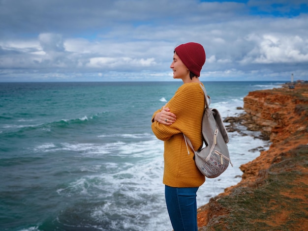 Mulher hipster viajante de suéter amarelo e chapéu vermelho desfrutando de ar fresco