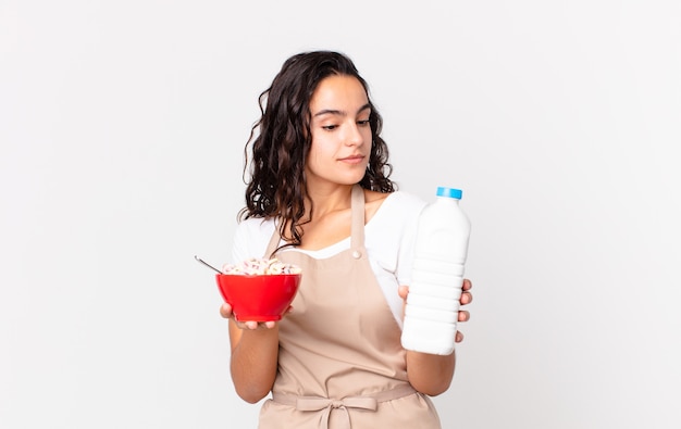 Mulher hispânica bonita chef segurando uma tigela de café da manhã com leite