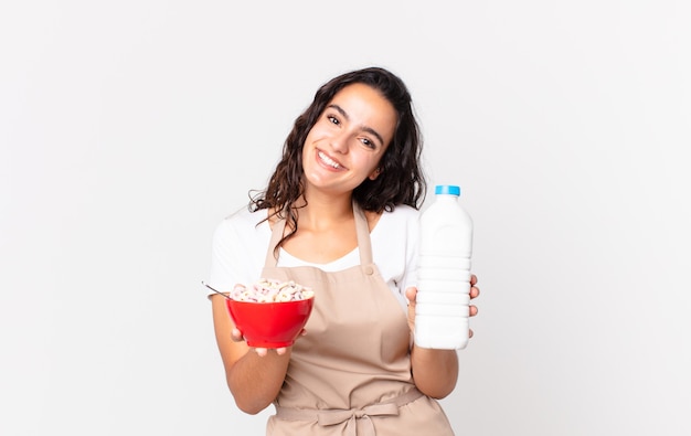 Mulher hispânica bonita chef segurando uma tigela de café da manhã com leite