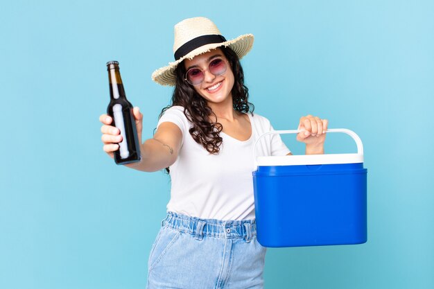 Mulher hispânica bonita com uma geladeira portátil e uma garrafa de cerveja