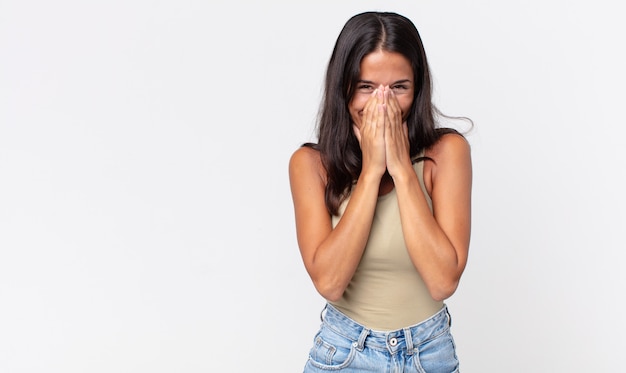 Mulher hispânica bonita e magrinha parecendo feliz cobrindo a boca com as duas mãos