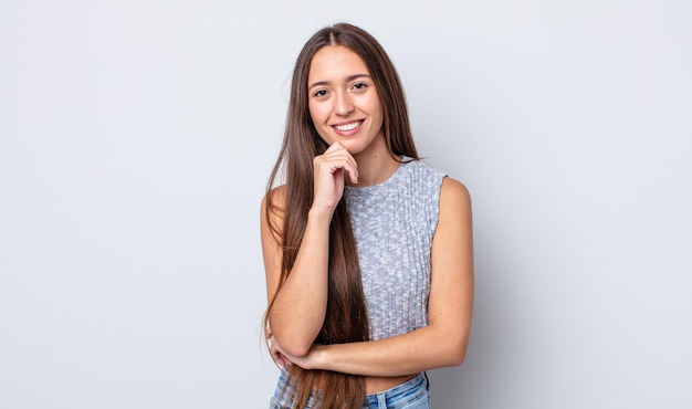 Mulher hispânica bonita parecendo feliz e sorrindo com a mão no queixo, pensando ou fazendo uma pergunta, comparando opções