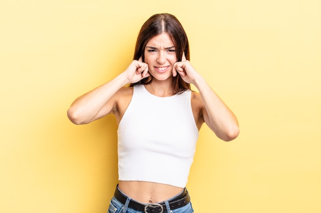 Mulher hispânica bonita parecendo zangada, estressada e irritada, cobrindo ambos os ouvidos para um barulho, som ou música alta ensurdecedores