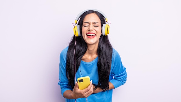 Mulher hispânica bonita rindo alto de alguma piada hilária. conceito de smartphone e fones de ouvido