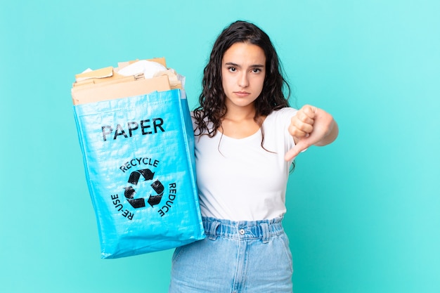 Mulher hispânica bonita se sentindo mal, mostrando os polegares para baixo e segurando um saco de papel reciclado