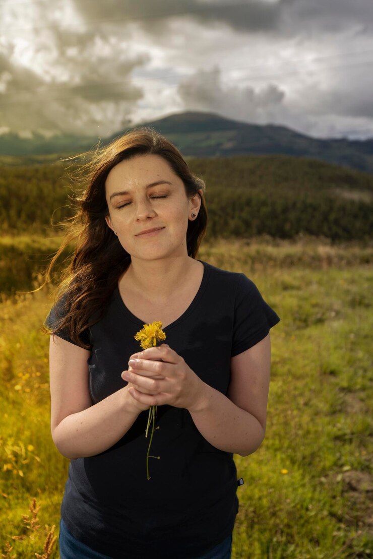 Foto mulher hispânica com os olhos fechados de pé no meio do campo cheirando flores amarelas