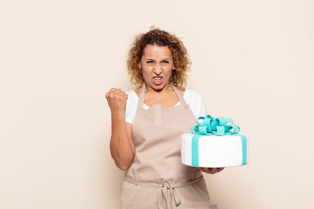 Mulher hispânica de meia-idade gritando agressivamente com uma expressão de raiva ou com os punhos cerrados celebrando o sucesso