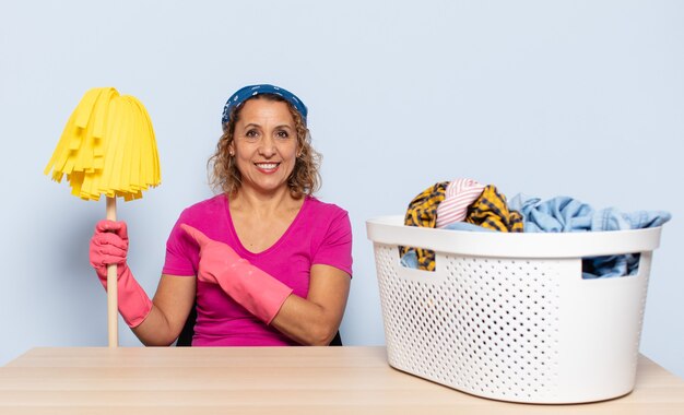 Foto mulher hispânica de meia idade sorrindo alegremente, sentindo-se feliz e apontando para o lado e para cima, mostrando o objeto no espaço da cópia