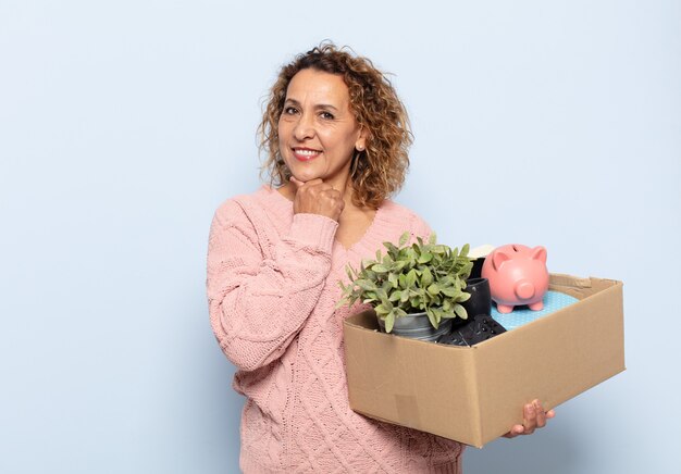 Mulher hispânica de meia-idade sorrindo com uma expressão feliz e confiante com a mão no queixo, pensando e olhando para o lado