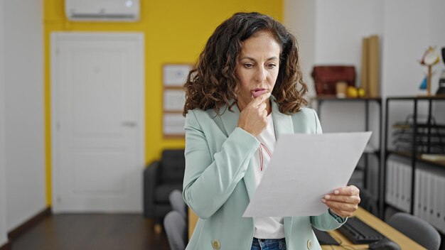 Foto mulher hispânica de meia-idade, trabalhadora de negócios, lendo documento com expressão de dúvida no escritório