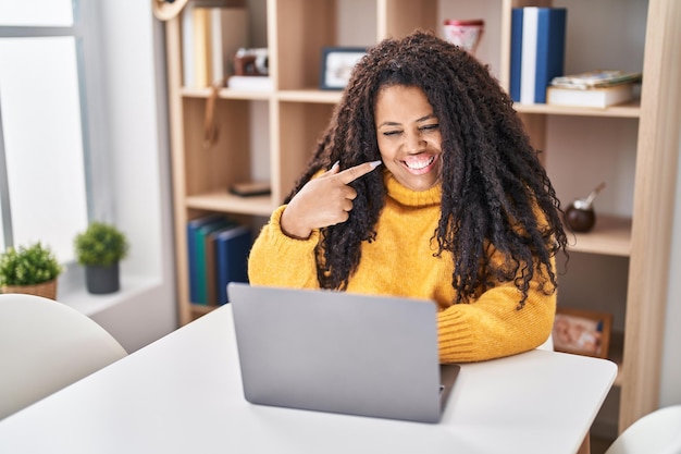 Mulher hispânica de tamanho grande usando laptop em casa sorrindo feliz apontando com a mão e o dedo