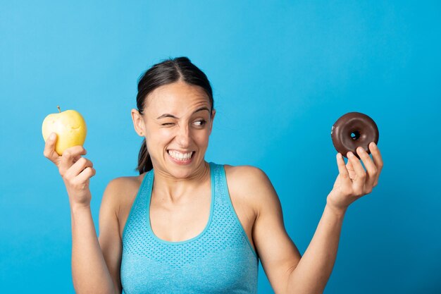 Mulher hispânica em forma, escolhendo entre frutas e rosquinha de chocolate