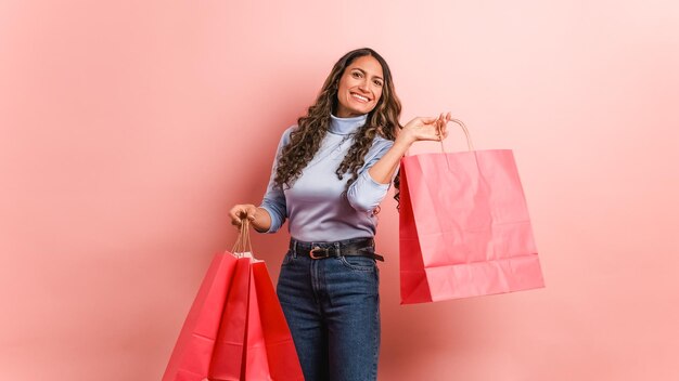 Mulher hispânica feliz mostrando sacos de compras cor-de-rosa