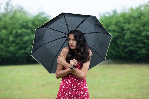 Mulher hispânica insatisfeita congelando sob o guarda-chuva na natureza