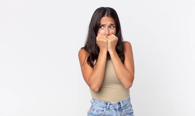 Mulher hispânica muito magra parecendo preocupada, roendo as unhas e olhando para o lado