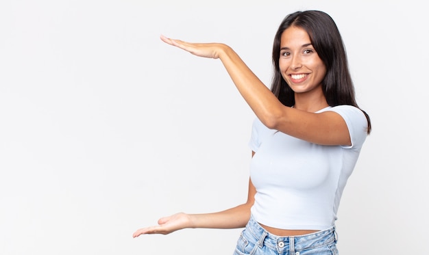 Mulher hispânica muito magra sorrindo, se sentindo feliz e segurando ou mostrando um conceito