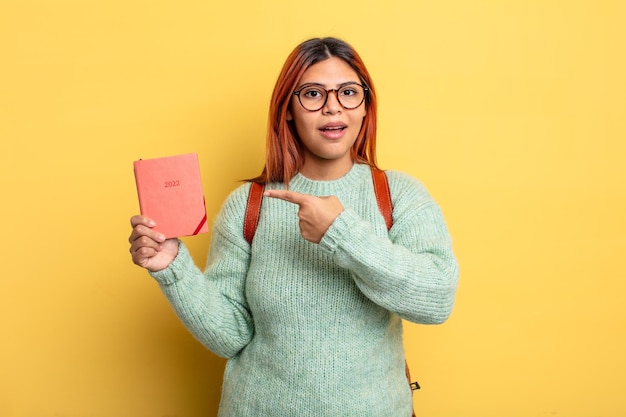 Mulher hispânica olhando animada e surpresa apontando para o lado. conceito de estudante e calendário