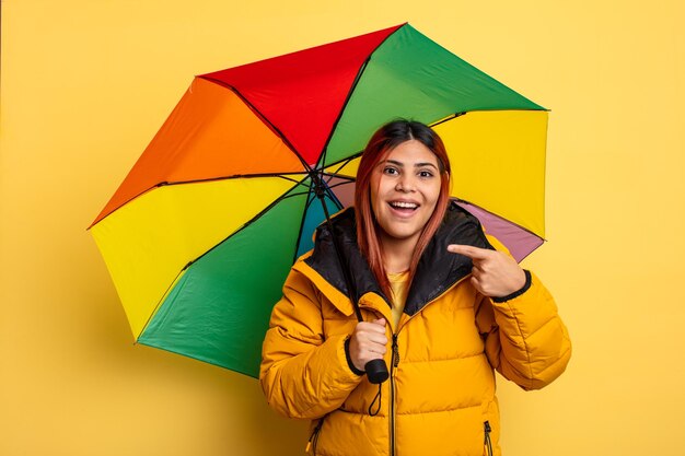 Mulher hispânica parecendo animada e surpresa apontando para o conceito de chuva e guarda-chuva lateral