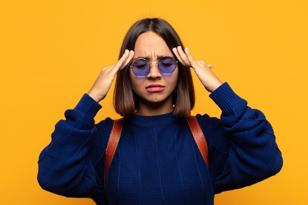 Mulher hispânica parecendo concentrada, pensativa e inspirada, fazendo um brainstorming e imaginando com as mãos na testa