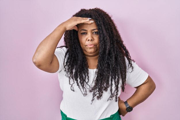 Mulher hispânica plus size em pé sobre fundo rosa preocupada e estressada com um problema com a mão na testa nervosa e ansiosa por crise