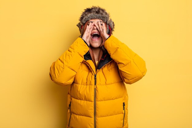 Mulher hispânica se sentindo feliz, dando um grande grito com as mãos ao lado da boca. conceito de inverno