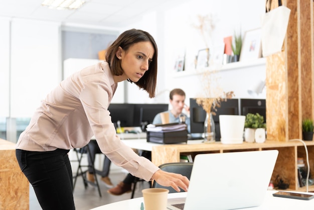 Mulher hispânica séria espionando o laptop de seu colega de trabalho no escritório.