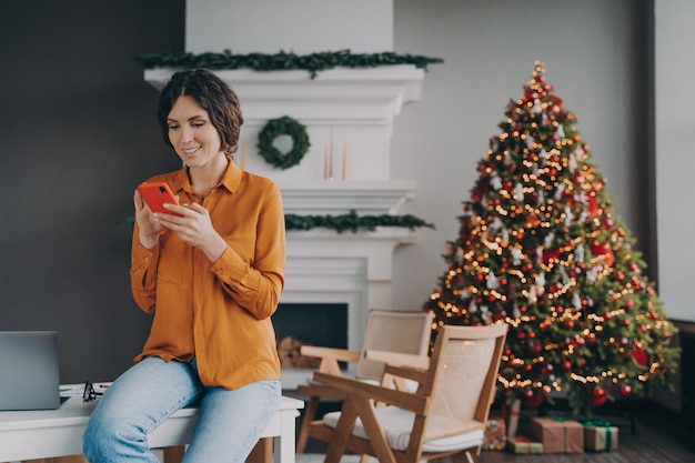 Mulher hispânica sorridente usando telefone celular durante o trabalho remoto em casa nas férias de Natal